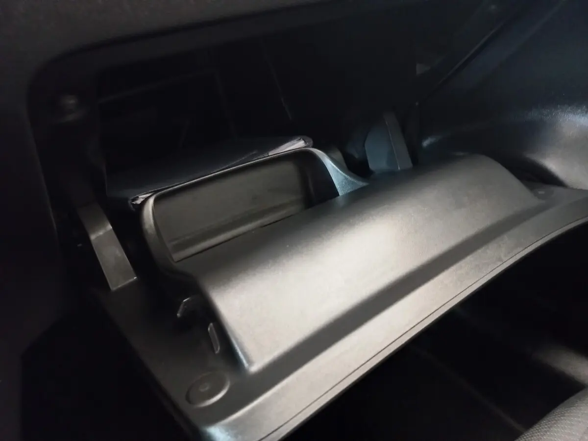 Gros plan sur la boîte à gants ouverte de la Peugeot 208 noire, intérieur sombre avec documents visibles.