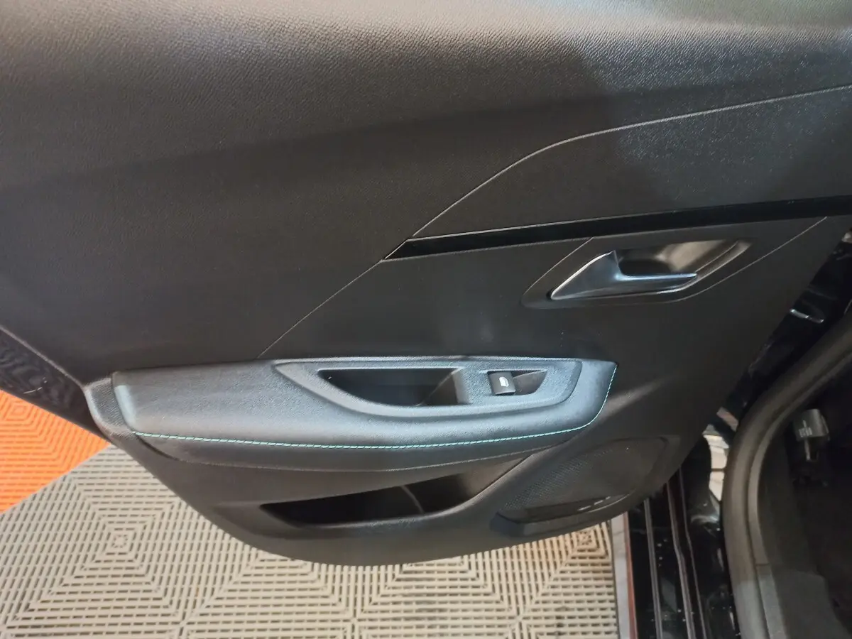 Gros plan sur la porte intérieure côté gauche noire de la Peugeot 208 PureTech 100 Allure Pack avec surpiqûres bleues.