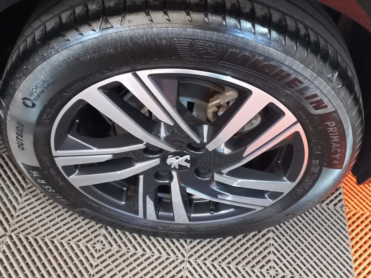 Gros plan sur la jante alliage noire et argentée d'une Peugeot 208 noire, avec pneu Michelin visible.