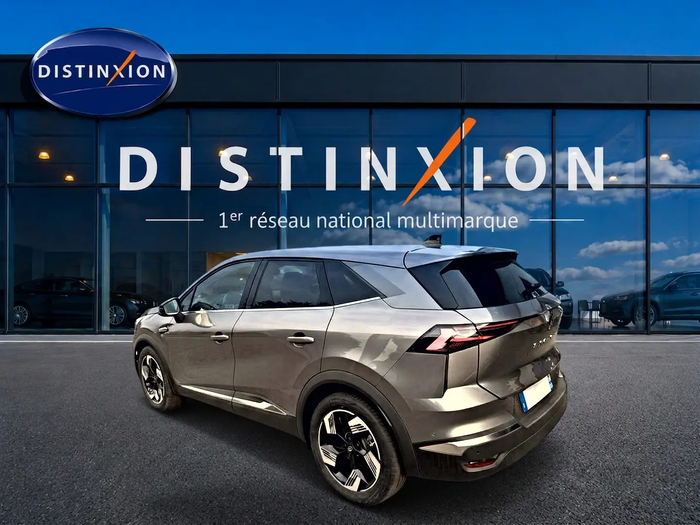 Vue 3/4 arrière droite d'un Renault Symbioz gris cassiopée avec jantes alu et feux arrière LED, devant un bâtiment Distinxion.