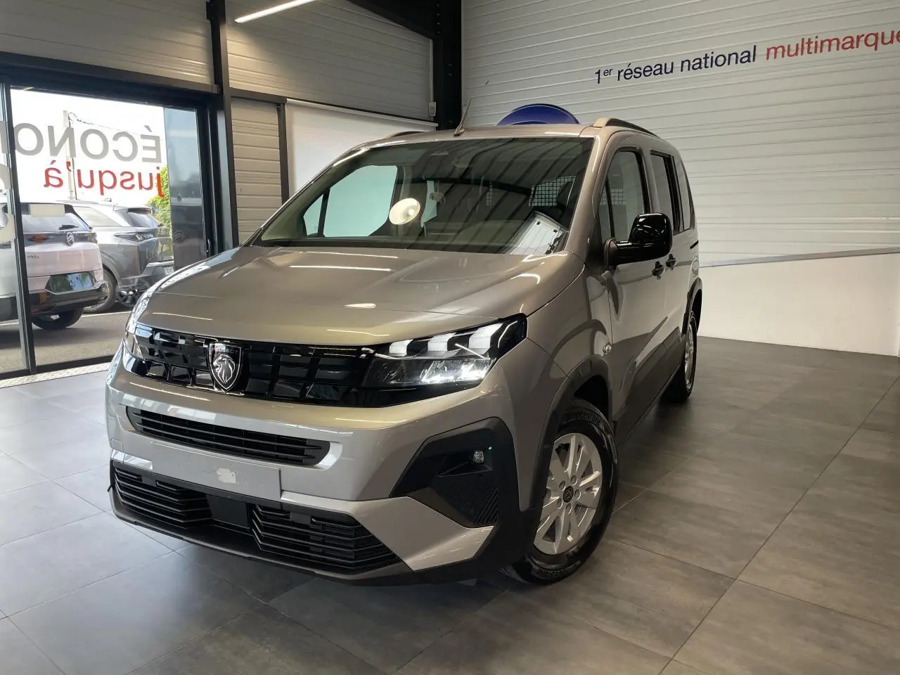 Peugeot Rifter gris Artense en 3/4 avant droit, avec calandre noire et jantes tôles 16 pouces en showroom.