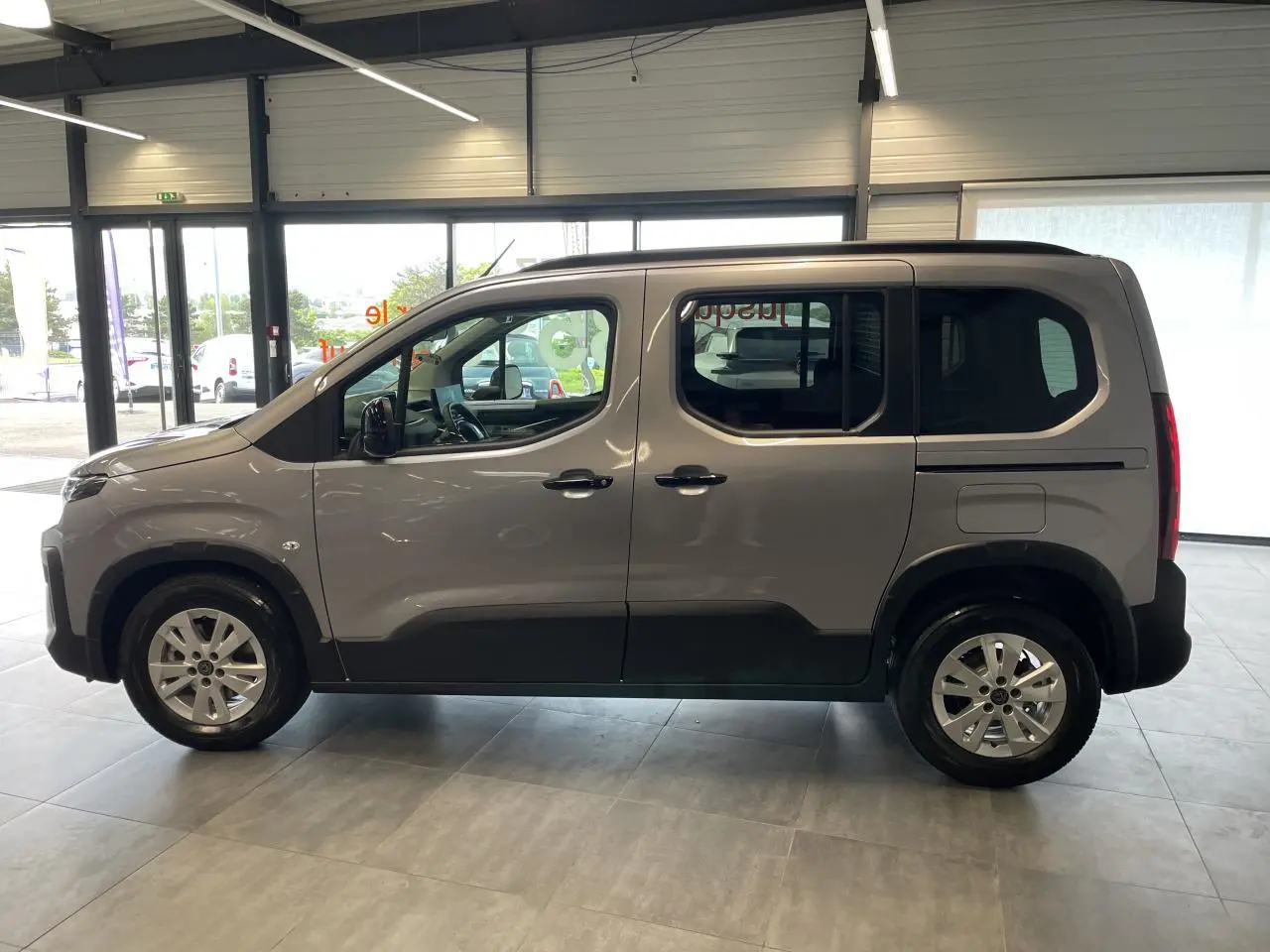 Profil côté gauche du Peugeot Rifter gris Artense 2026 avec portes coulissantes et jantes tôles 16 pouces en showroom.
