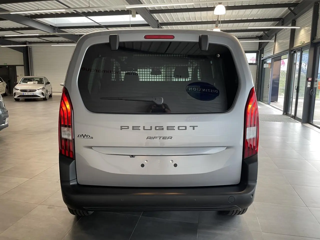 Vue arrière d’un Peugeot Rifter gris Artense avec feux verticaux LED et pare-chocs noir mat en showroom.