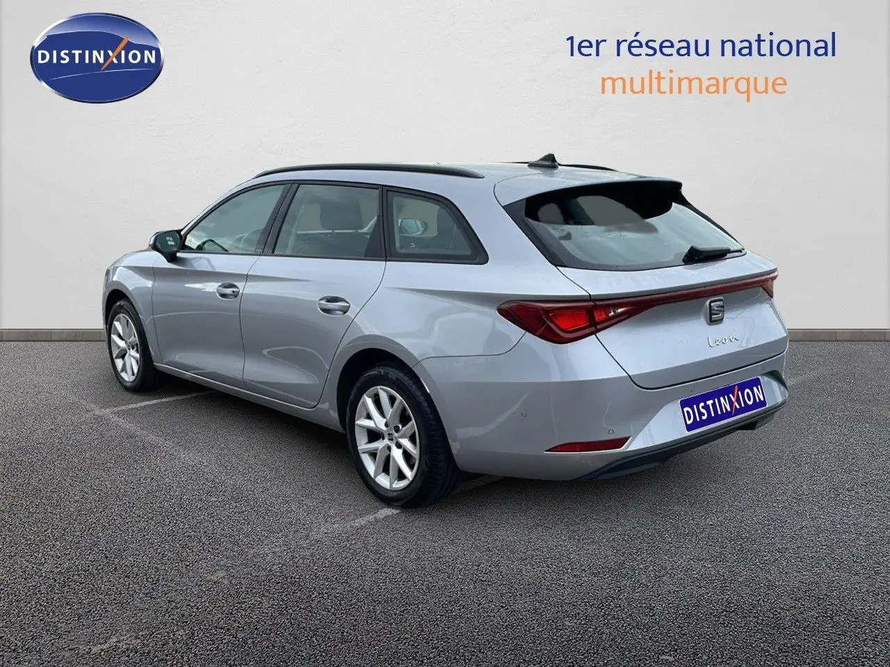 SEAT Leon ST gris urbain vue 3/4 arrière côté gauche, break compact avec feux arrière reliés par un bandeau lumineux.