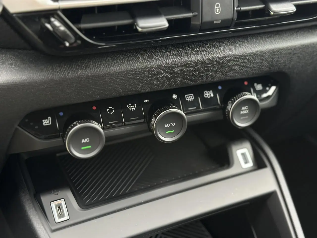 Gros plan sur la console centrale noire de la Citroën C4 2025, montrant les commandes de climatisation automatique et USB.