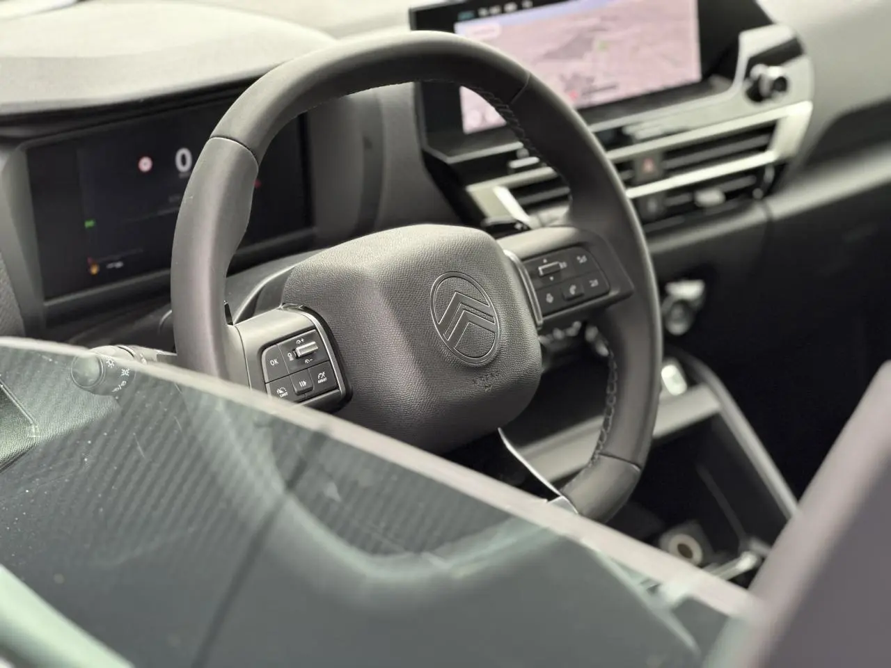Vue rapprochée du volant cuir noir de la Citroën C4 NV Hybrid 2025 avec tableau de bord numérique et écran tactile central.