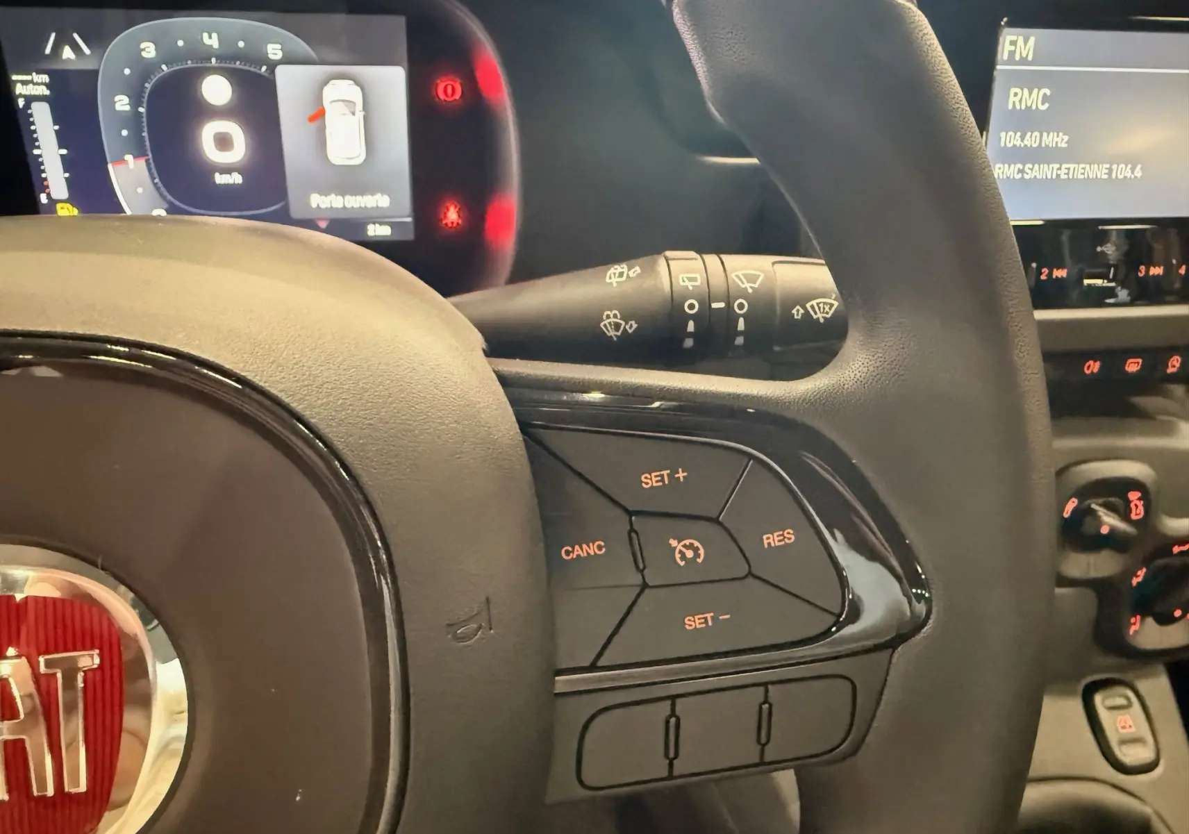 Vue rapprochée du volant noir de la Fiat Panda 2025 avec commandes de régulateur de vitesse et tableau de bord numérique allumé.