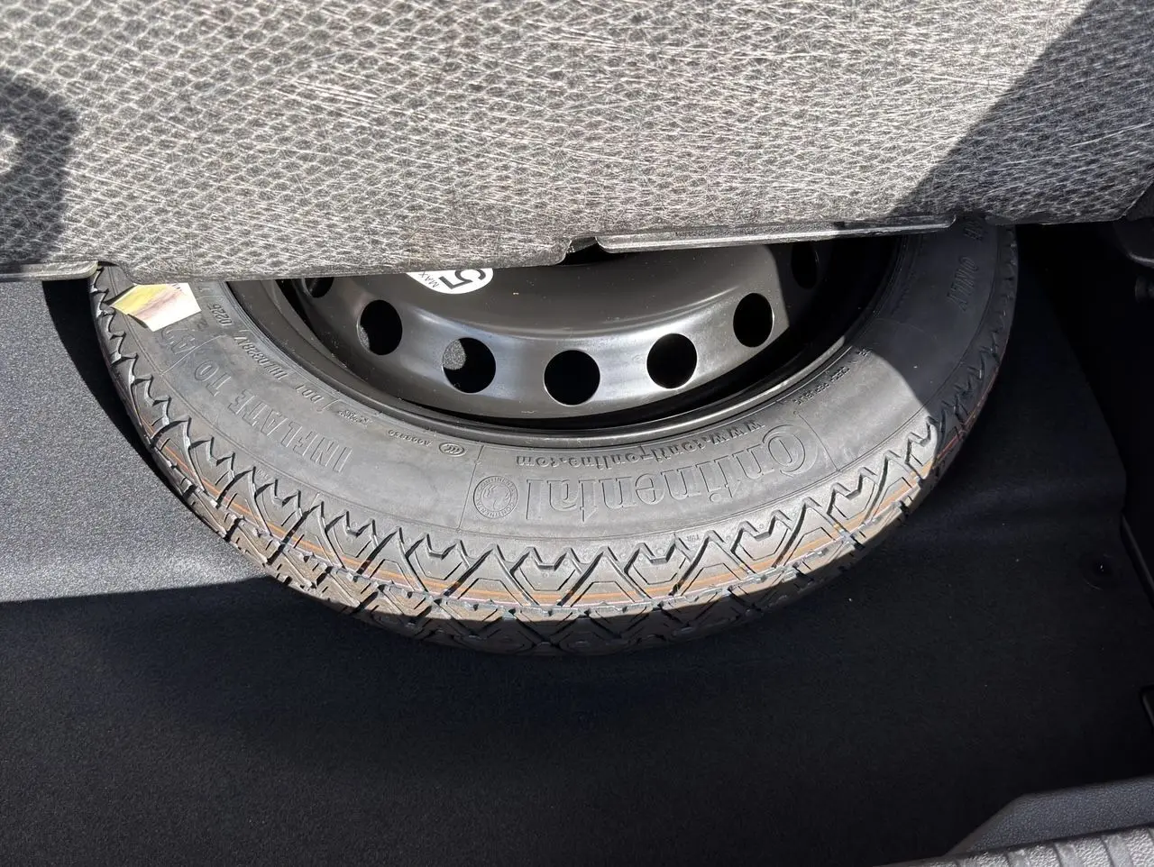 Gros plan sur la roue de secours noire dans le coffre du Renault Symbioz gris clair, visible sous la banquette arrière.