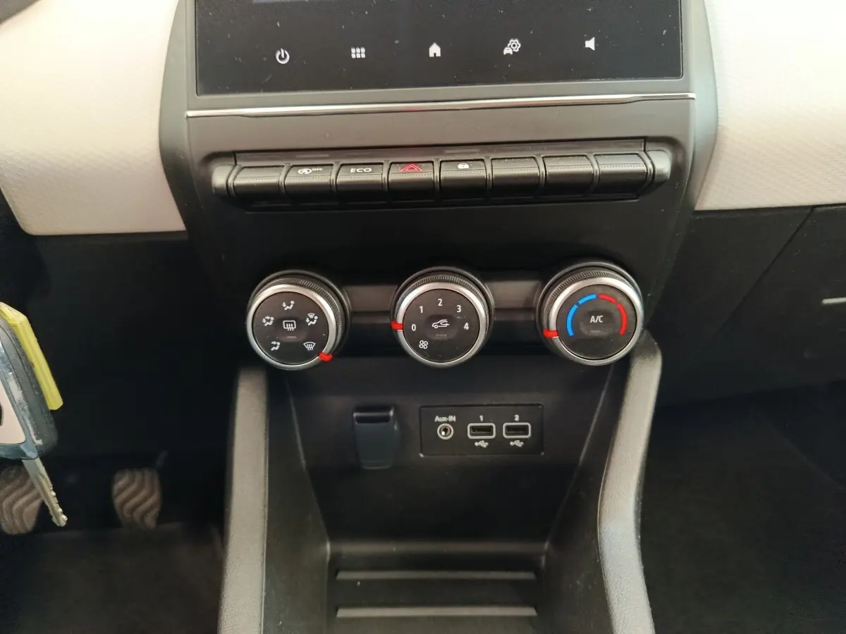 Vue rapprochée du tableau de bord central de la Renault Clio blanc, montrant les commandes de climatisation et ports USB.