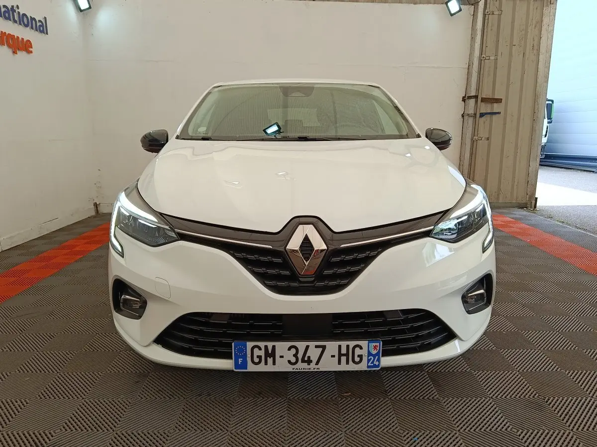 Vue de face d'une Renault Clio Evolution TCe 100 GPL blanche avec phares LED allumés dans un garage.