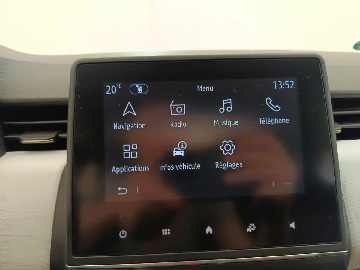 Écran tactile central de la Renault Clio blanc, affichant le menu principal avec navigation et musique.