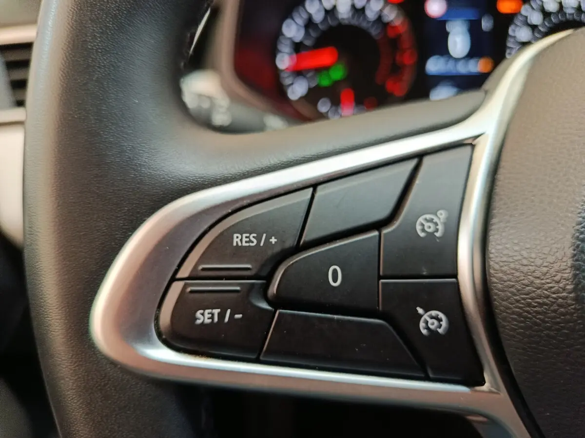 Gros plan sur les commandes du régulateur de vitesse au volant cuir synthétique de la Renault Clio blanche 2023.