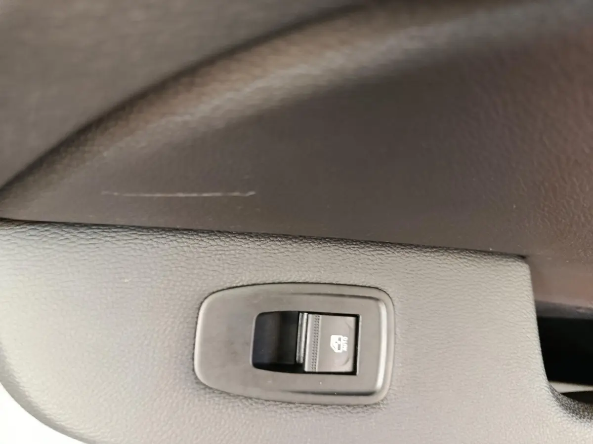 Gros plan sur le bouton de verrouillage des vitres arrière dans l’habitacle noir de la Renault Clio blanche.