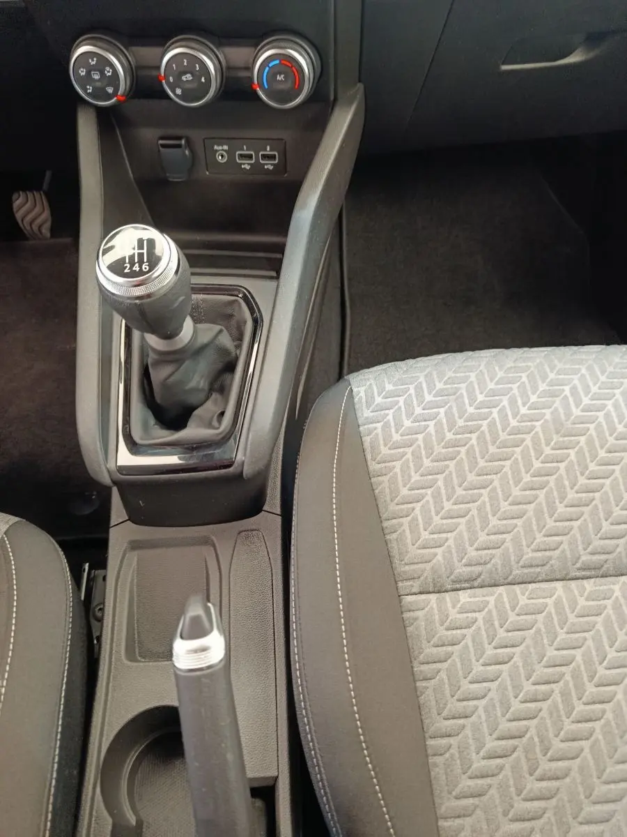 Vue rapprochée de la console centrale d'une Renault Clio blanche 2023, avec levier de vitesse manuel et siège tissu gris.