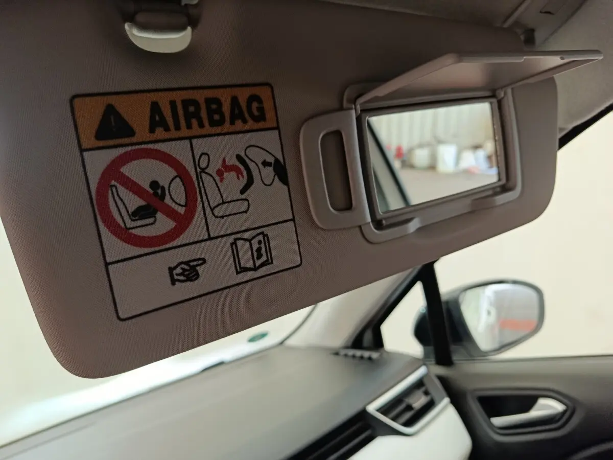 Détail intérieur de la Renault Clio blanc, miroir de pare-soleil côté conducteur avec avertissement airbag visible.