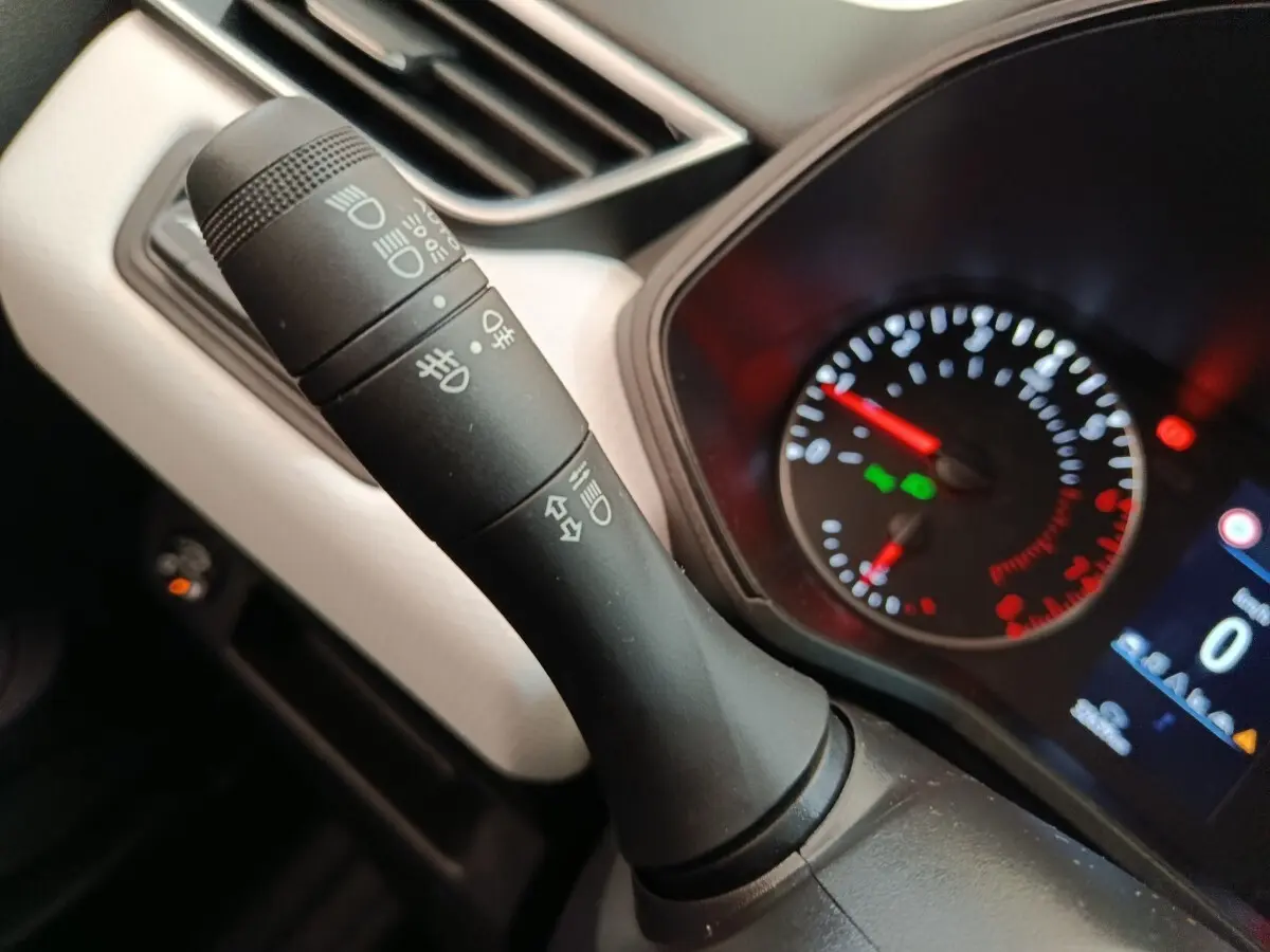 Gros plan sur la manette de commandes des phares et clignotants dans l'habitacle d'une Renault Clio blanche 2023.