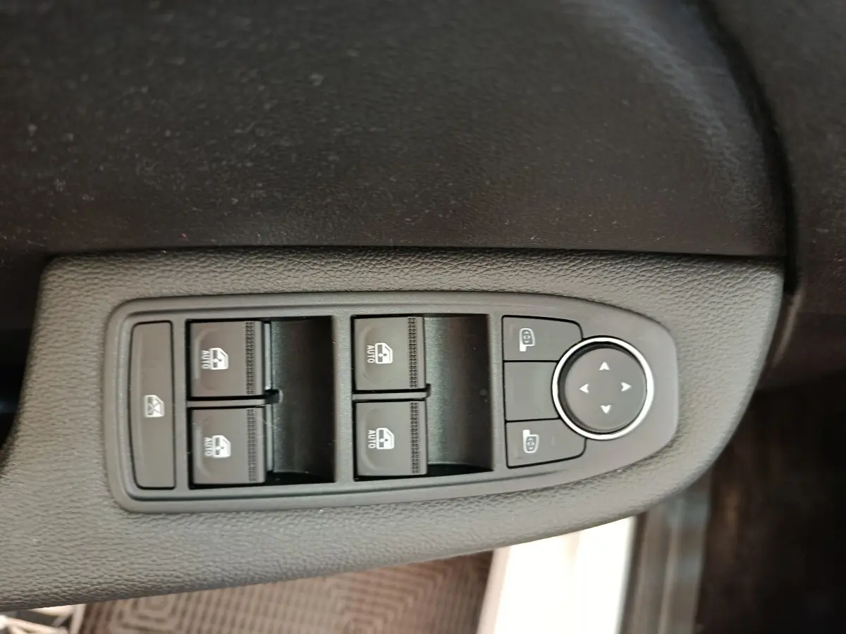 Gros plan sur les commandes des vitres électriques et rétroviseurs du côté conducteur d’une Renault Clio blanche Evolution TCe 100 GPL.