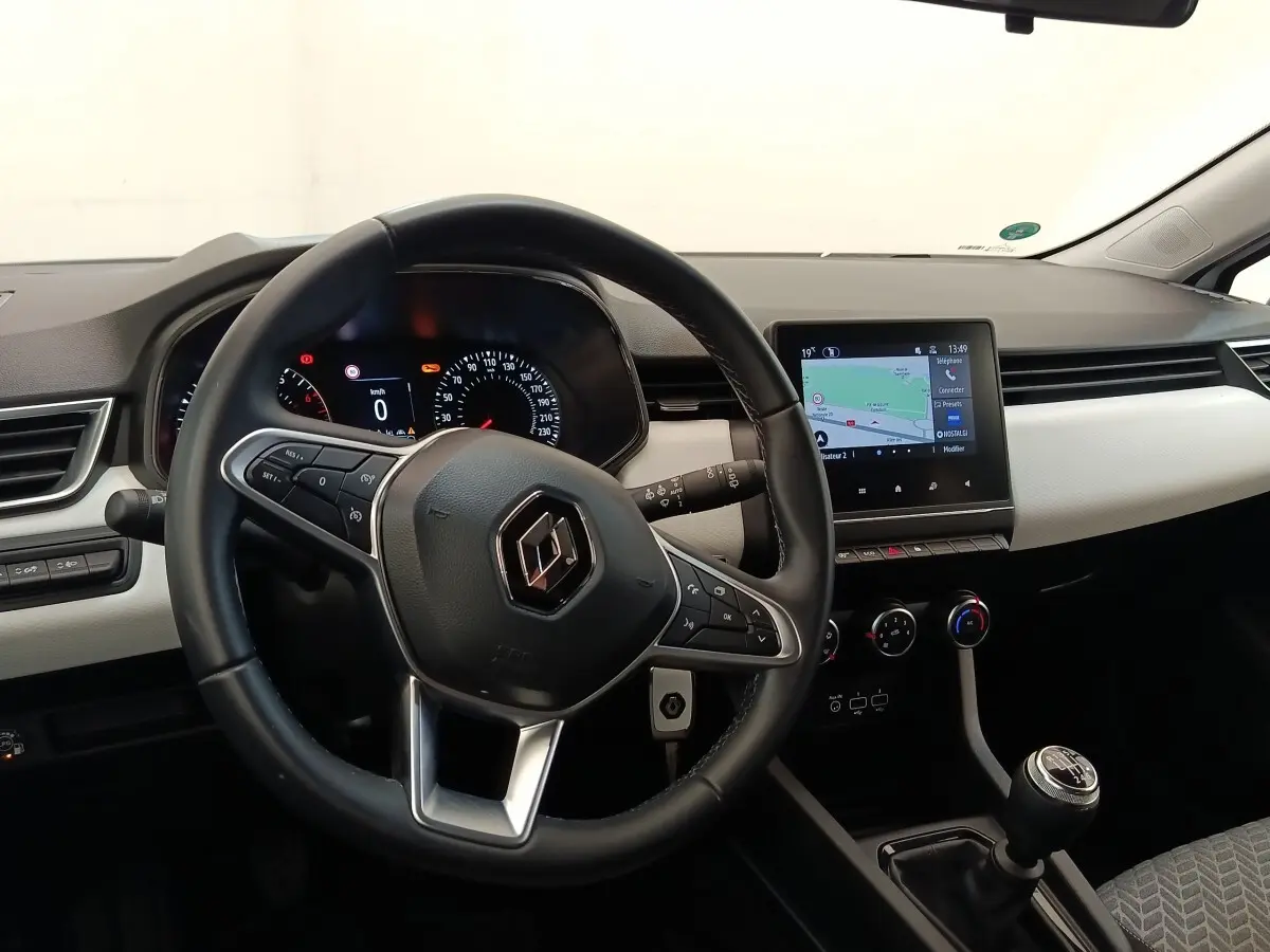 Vue intérieure de face du tableau de bord de la Renault Clio blanche, avec volant cuir, écran tactile et levier de vitesses manuel.