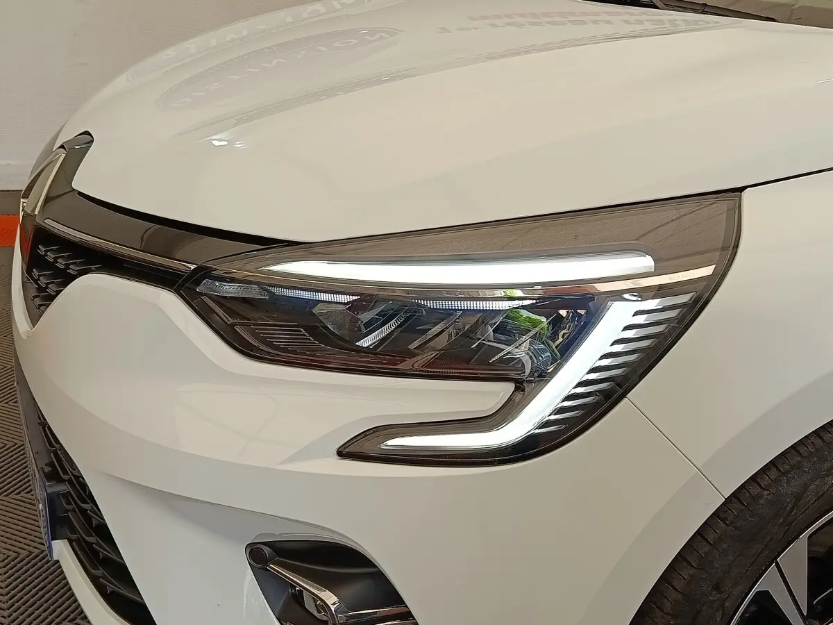 Gros plan sur le phare avant droit allumé d'une Renault Clio blanche Evolution TCe 100 GPL de 2023.