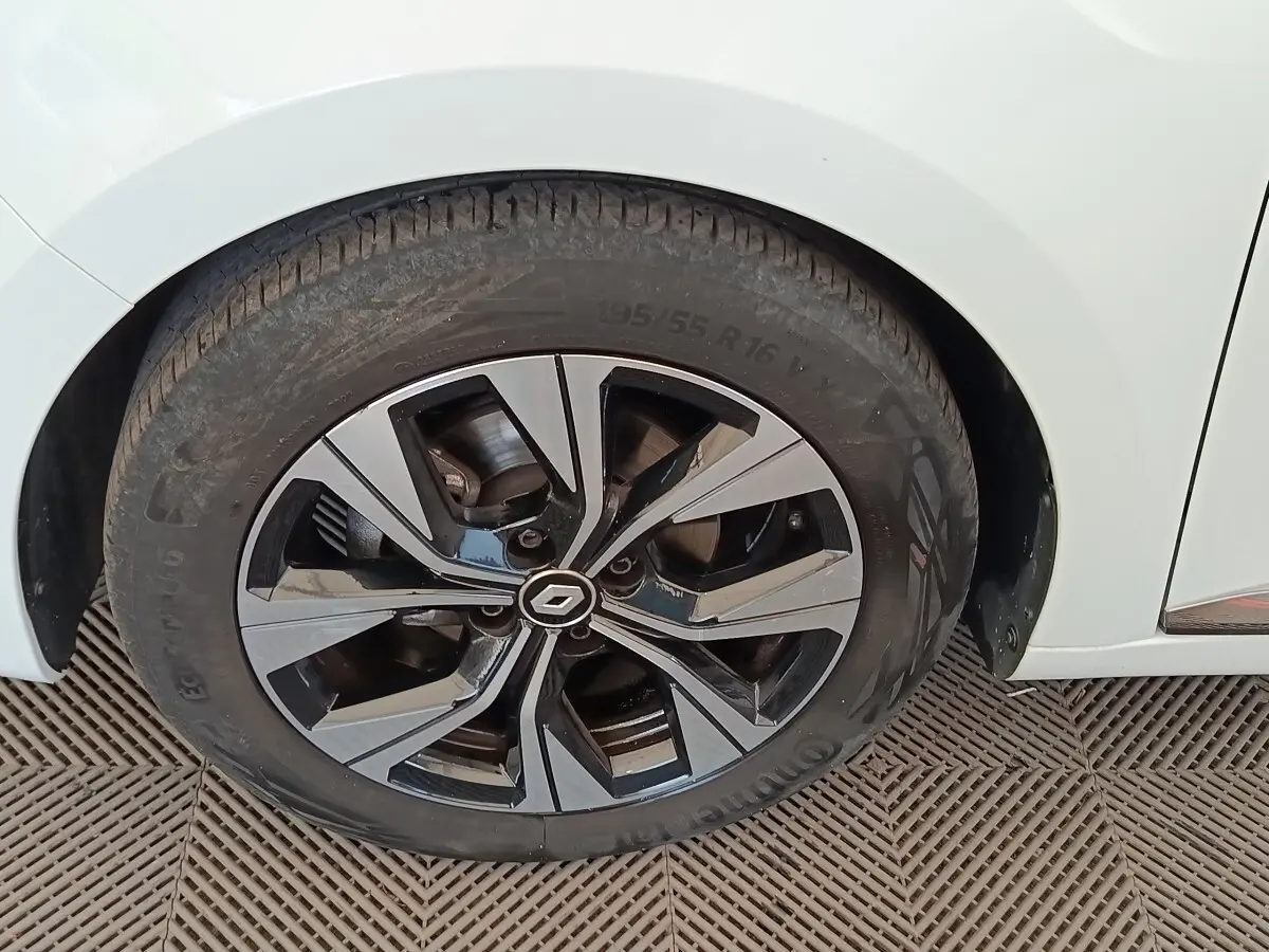 Gros plan sur la roue avant droite d’une Renault Clio blanche, avec jante alliage bicolore au design moderne.