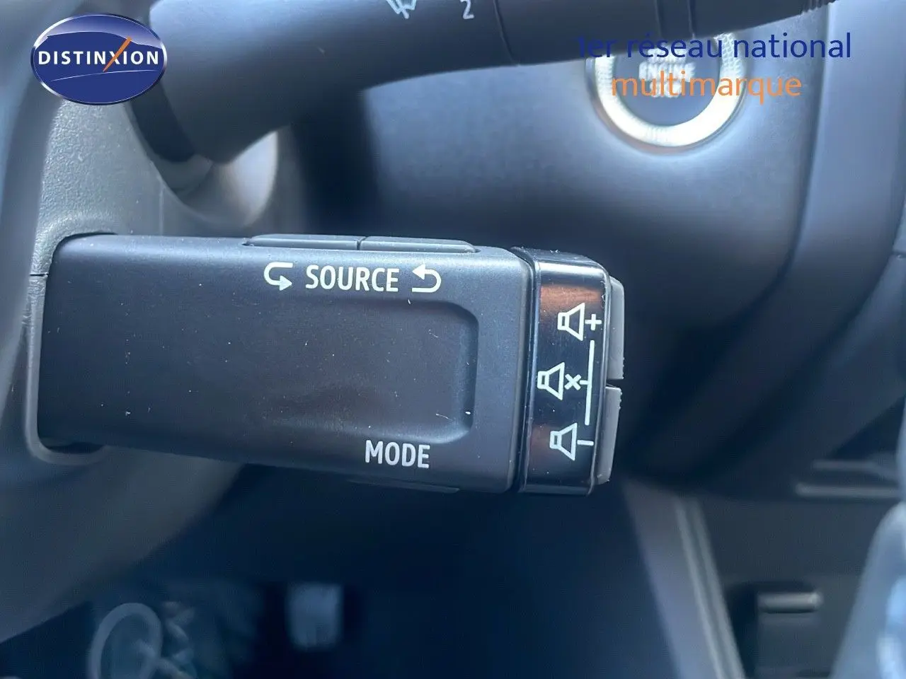 Gros plan sur la commande au volant du Renault Captur E-Tech hybride 2025 en noir étoile métal, avec boutons source et mode visibles.