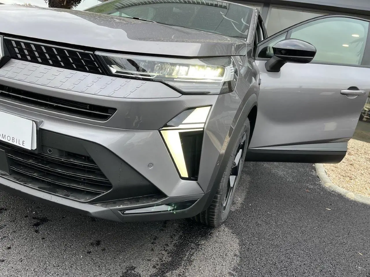 Vue avant droite du Renault Captur gris Cassiopée 2025 avec porte ouverte et éclairage LED allumé.