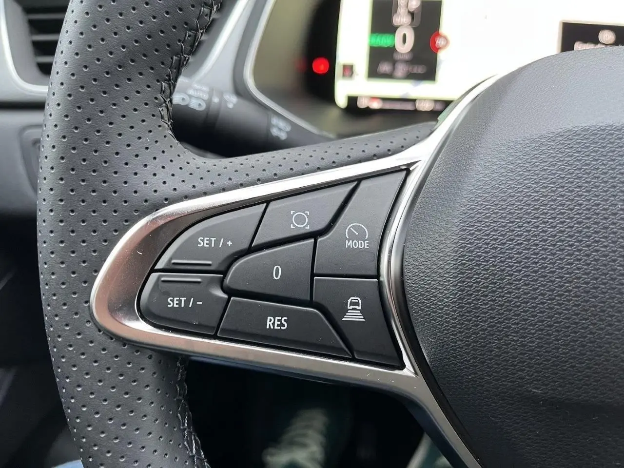 Gros plan sur les commandes au volant gauche du Renault Captur gris Cassiopée, version hybride 2025, avec boutons multifonctions.