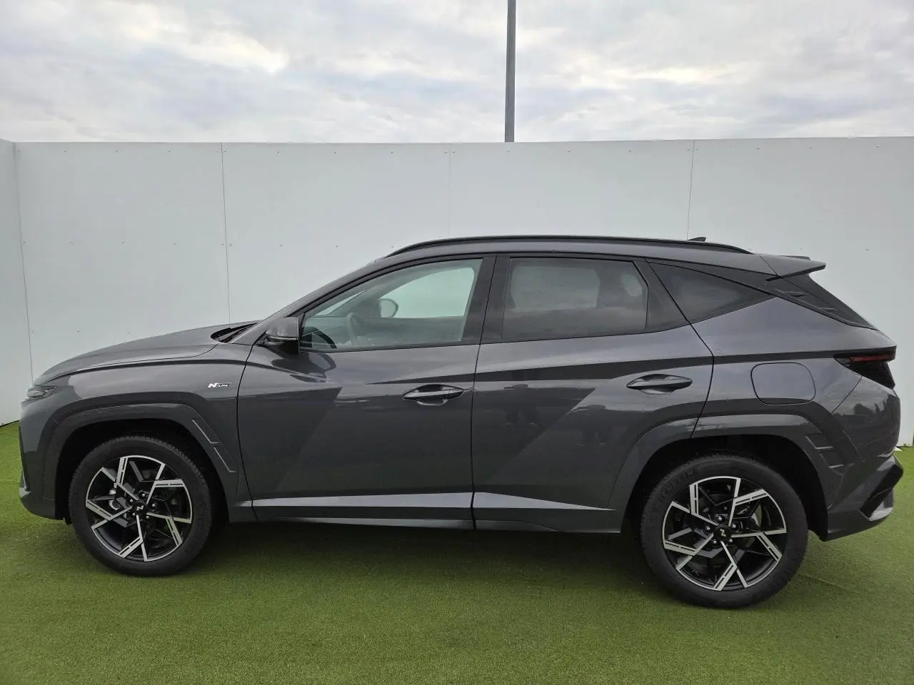 Vue latérale gauche du Hyundai Tucson 2025 en gris métallisé Ecotronic avec jantes alliage 19'' N Line et vitres surteintées.