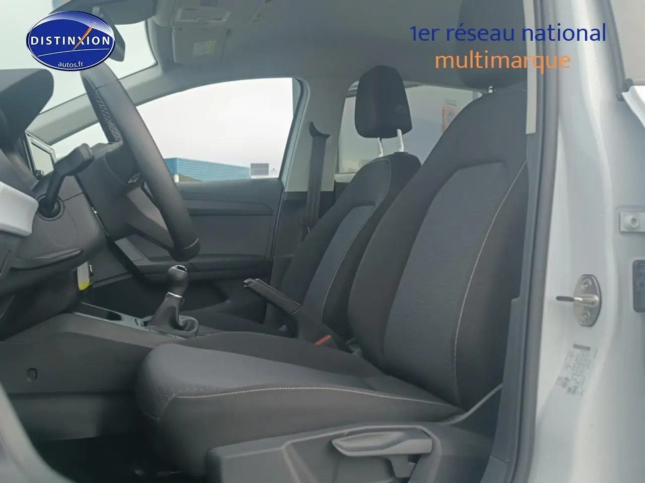 Vue intérieure côté conducteur de la SEAT Ibiza blanc Nevada 2025, sièges tissu gris et volant multifonction cuir.