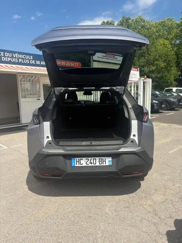 Vue arrière d'un Peugeot 3008 Hybrid gris clair 2025 avec coffre ouvert, montrant l'espace de chargement vide.