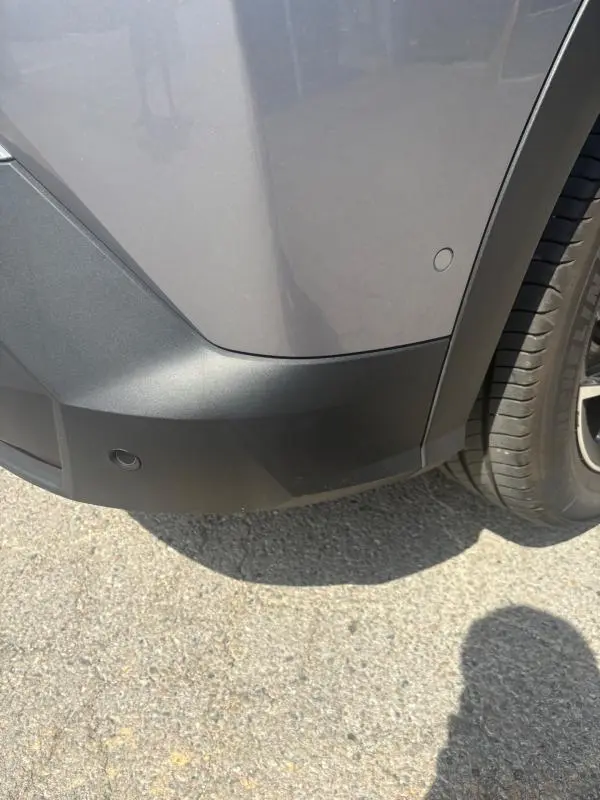 Détail de l'angle arrière droit du Peugeot 3008 Hybrid 136 e-DCS6 Allure gris clair avec pare-chocs noir et capteur de stationnement.