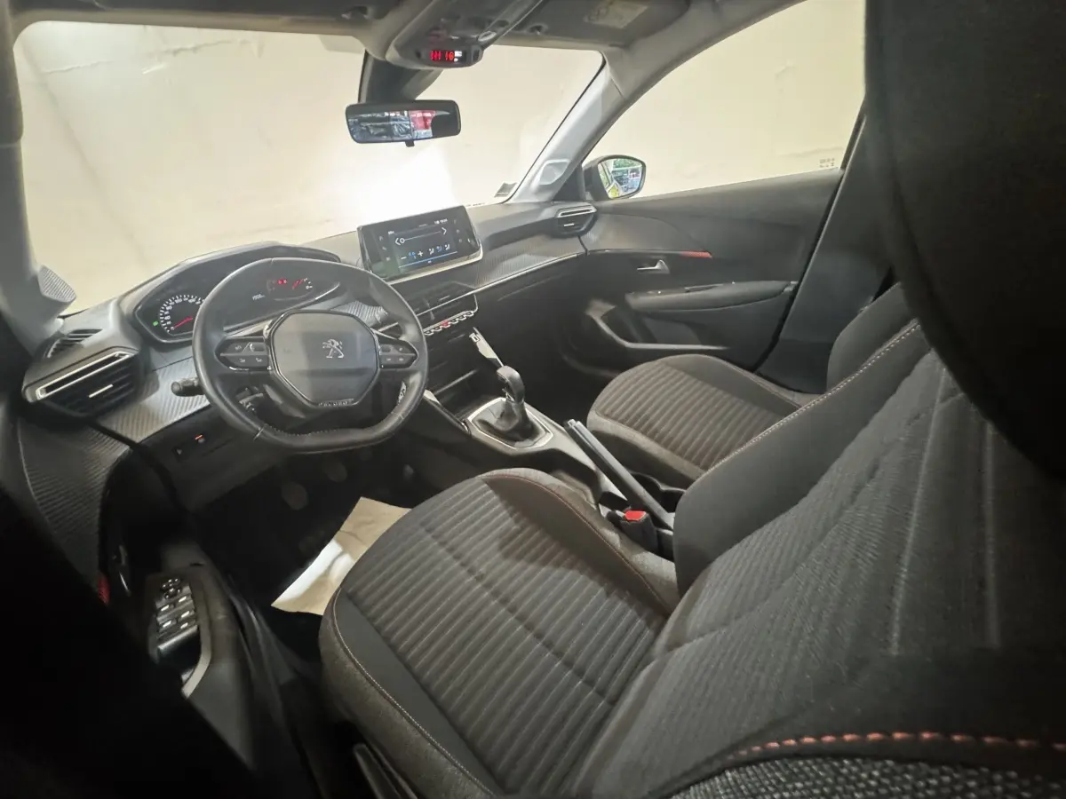 Vue intérieure côté conducteur de la Peugeot 208 PureTech 75 S&S Active Pack avec tableau de bord noir et volant cuir.