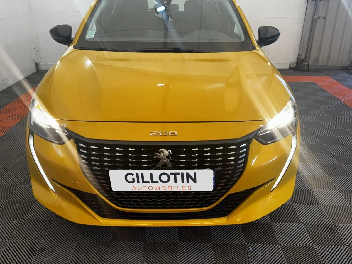 Vue frontale d'une Peugeot 208 jaune avec phares allumés et calandre noire distinctive.