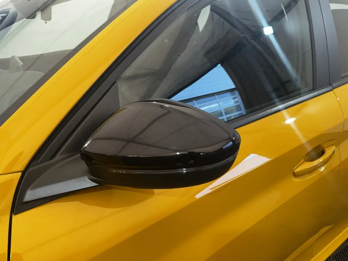 Rétroviseur noir en gros plan côté gauche sur Peugeot 208 jaune vif, avec reflet de l'environnement intérieur.