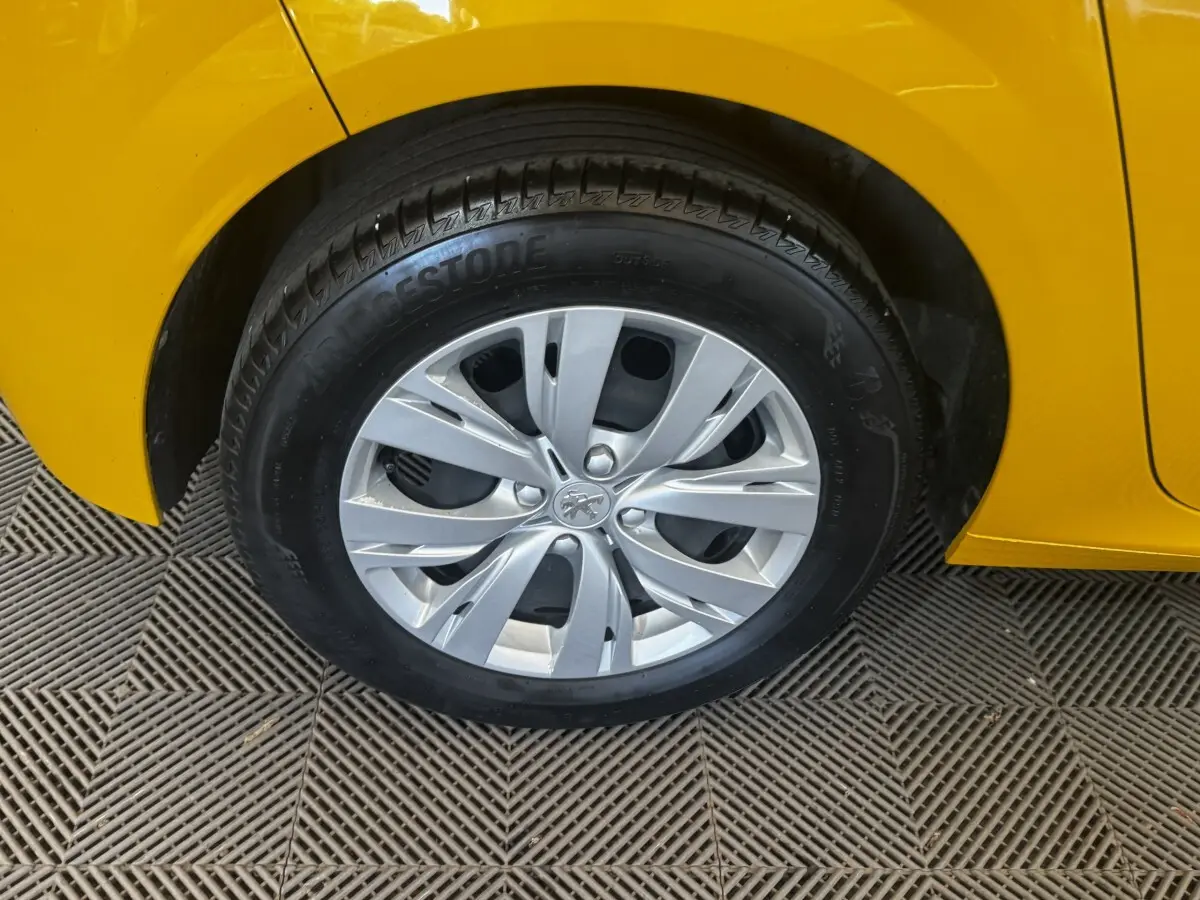 Gros plan sur la roue avant droite d’une Peugeot 208 jaune, jante en alliage argenté avec logo lion au centre.