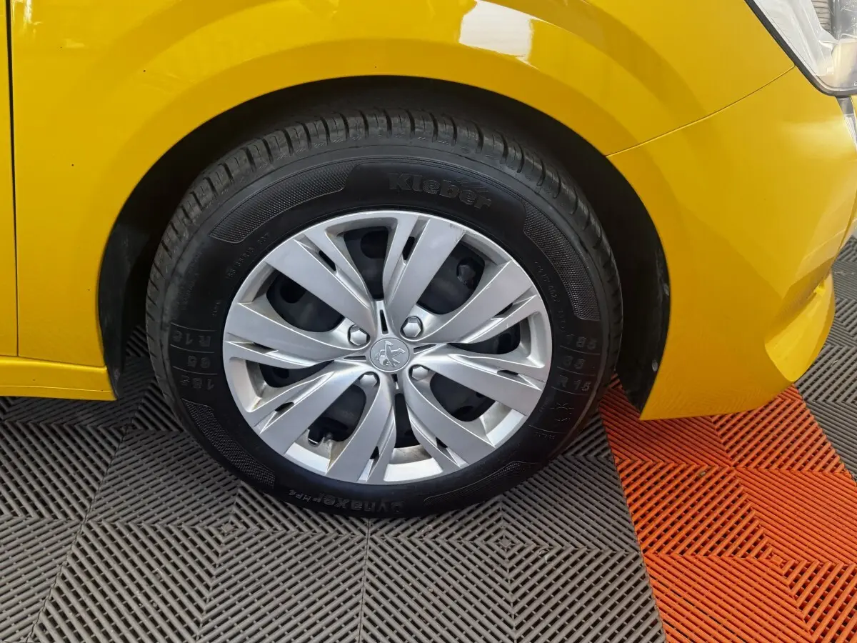 Gros plan sur la roue avant gauche d’une Peugeot 208 jaune 2023 avec jante alliage et pneu Kleber.
