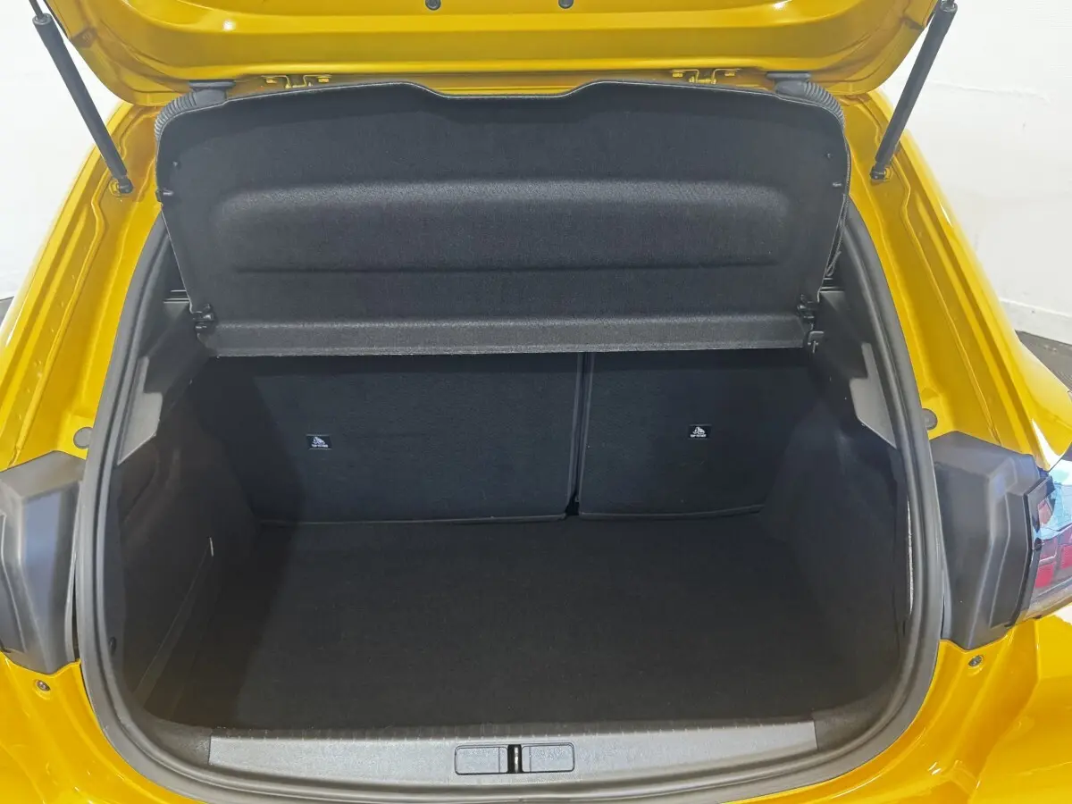 Coffre ouvert vu de l'arrière d'une Peugeot 208 jaune 2023, montrant l'espace de chargement vide et la tablette de séparation.