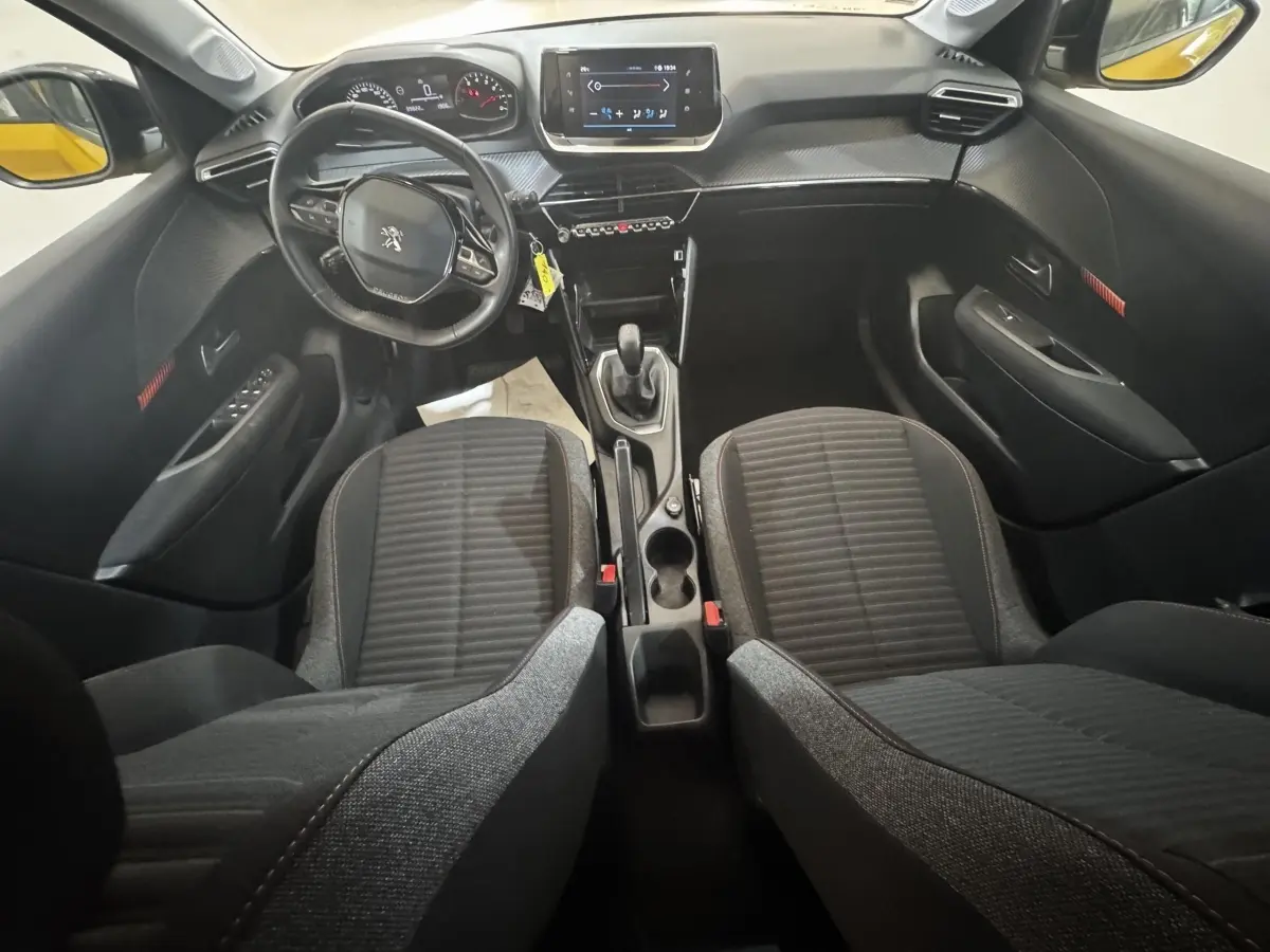 Vue intérieure avant de la Peugeot 208 jaune 2023, montrant le volant cuir, tableau de bord et écran tactile central.