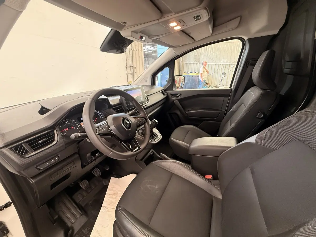 Vue intérieure côté conducteur du Renault Kangoo 2023, volant multifonctions et sièges noirs en tissu et cuir.