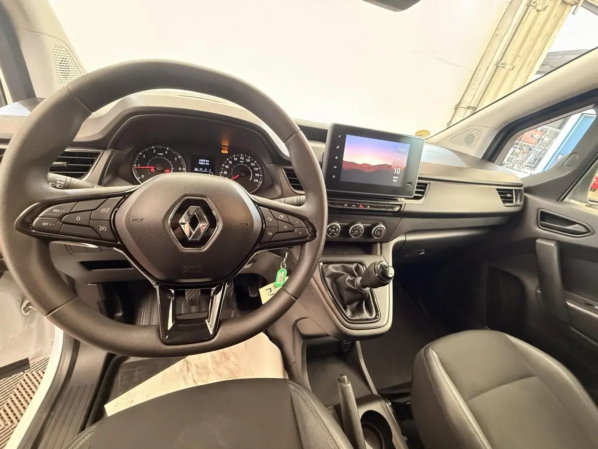 Vue intérieure avant du Renault Kangoo blanc 2023, volant multifonctions et écran tactile central visible.