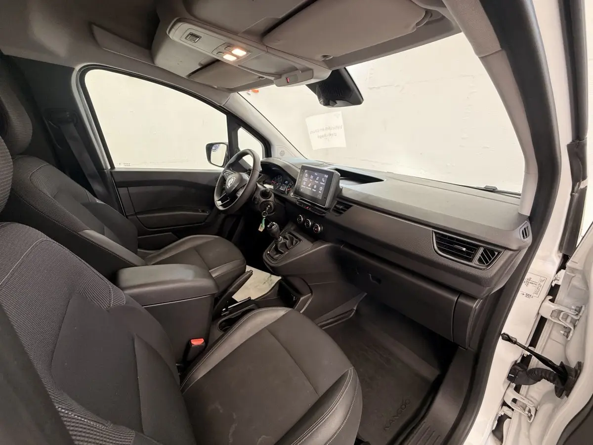 Vue intérieure côté droit du Renault Kangoo blanc 2023, montrant le tableau de bord et les sièges avant noirs.