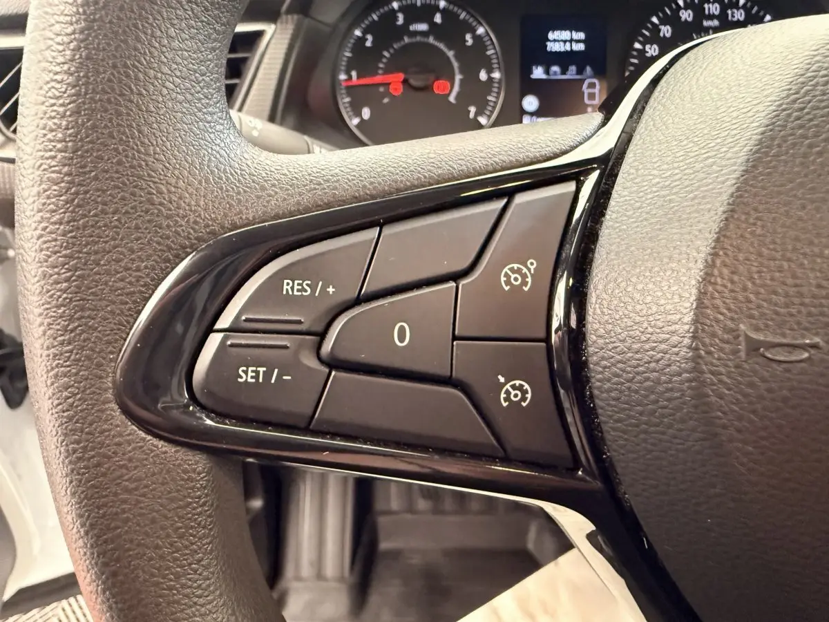 Gros plan sur le volant multifonctions noir du Renault Kangoo blanc, avec commandes de régulateur de vitesse visibles.