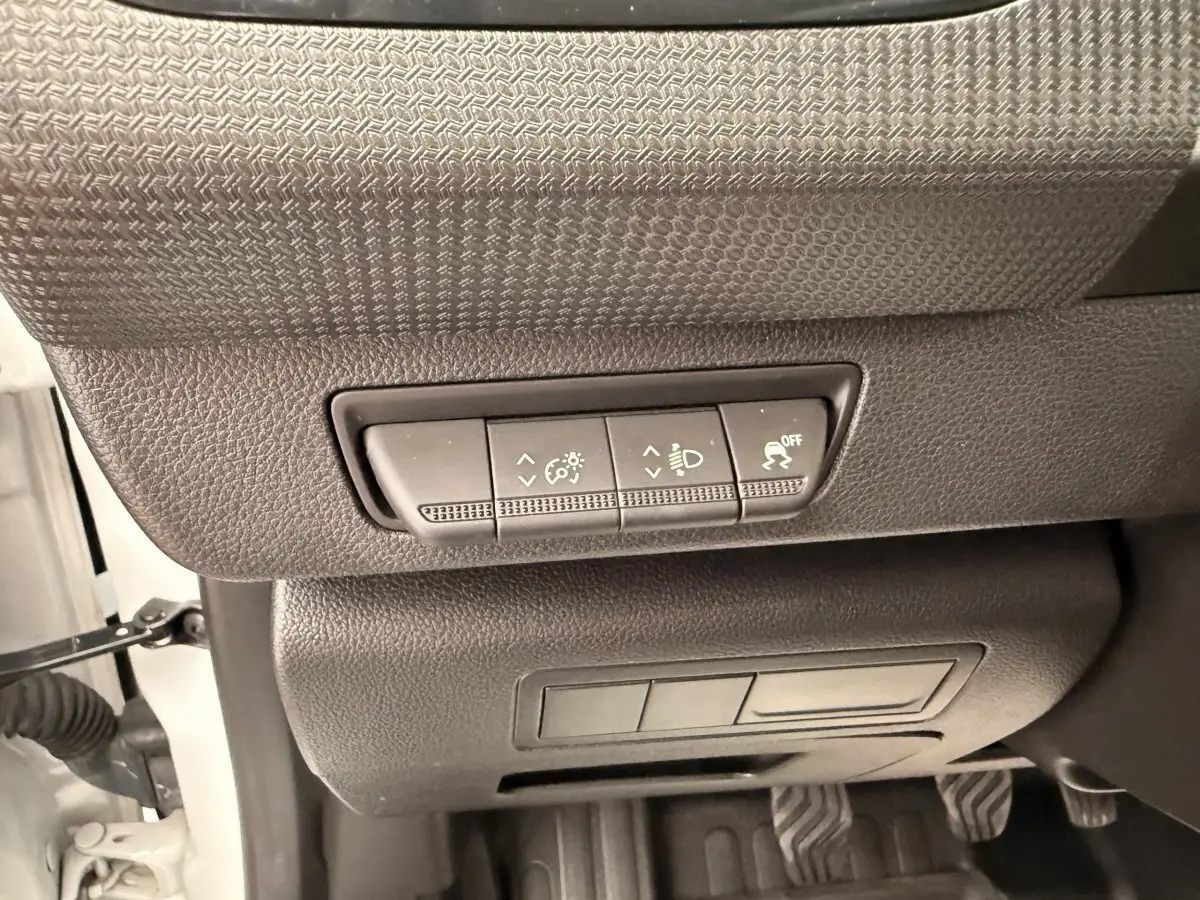 Gros plan sur les commandes de réglage des phares et antipatinage sous le tableau de bord d’un Renault Kangoo blanc.