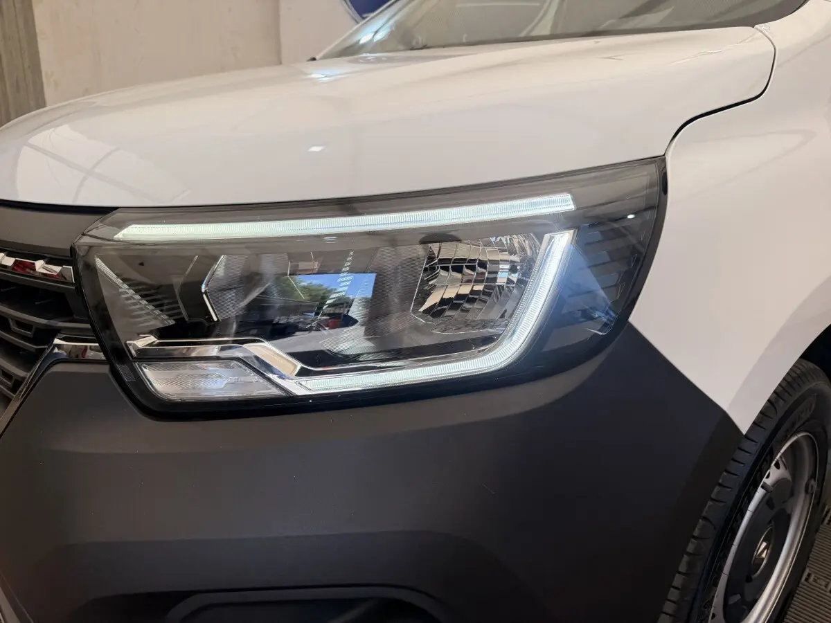 Gros plan sur le phare avant droit du Renault Kangoo blanc 2023 avec éclairage LED et pare-chocs noir mat.