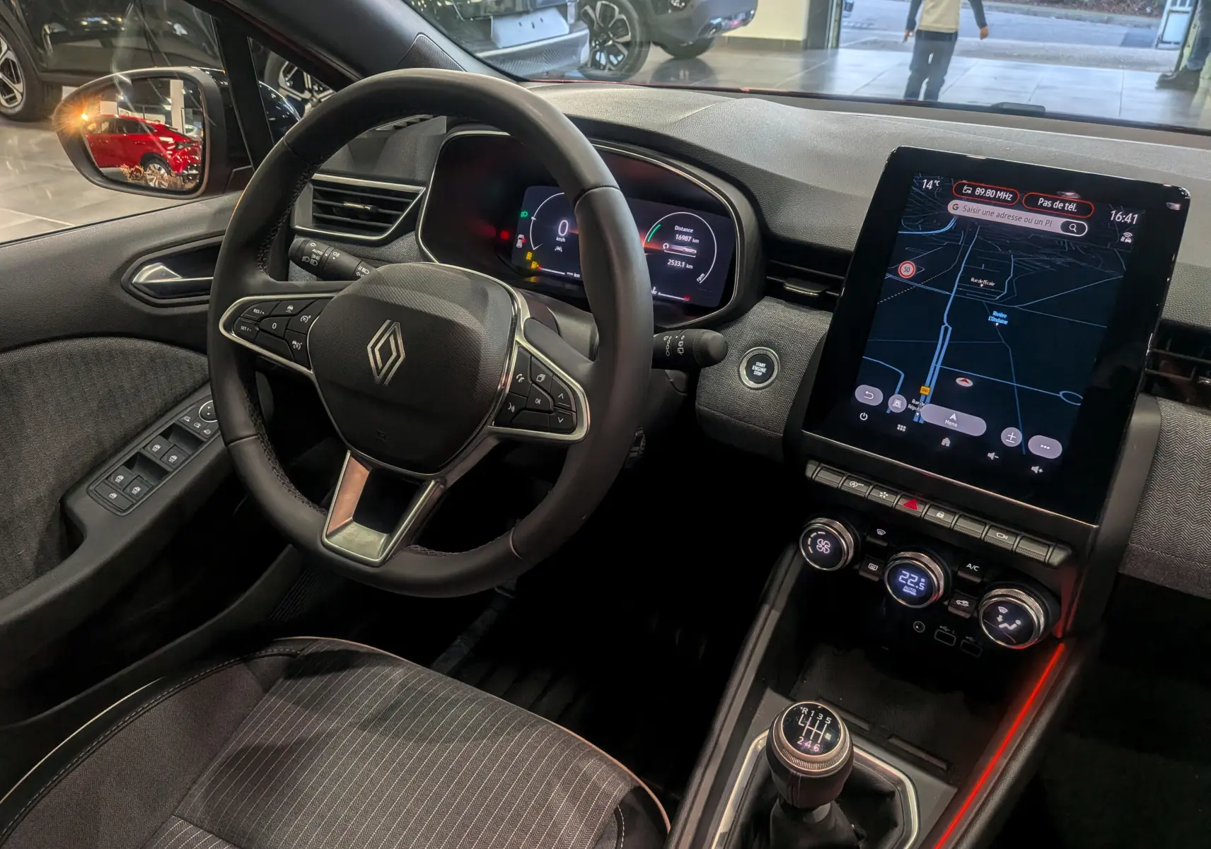 Vue intérieure côté conducteur de la Renault Clio V Rouge Flamme, avec tableau de bord digital et écran tactile vertical.