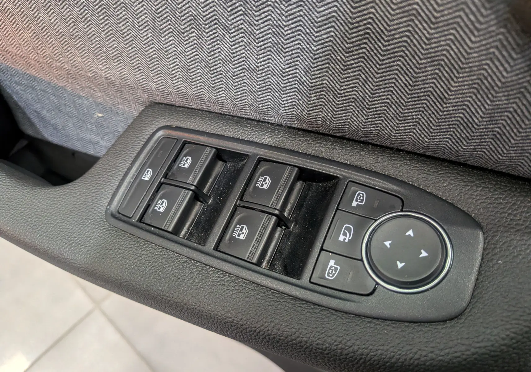 Gros plan sur les commandes électriques des vitres et rétroviseurs côté gauche intérieur d’une Renault Clio V rouge Flamme.