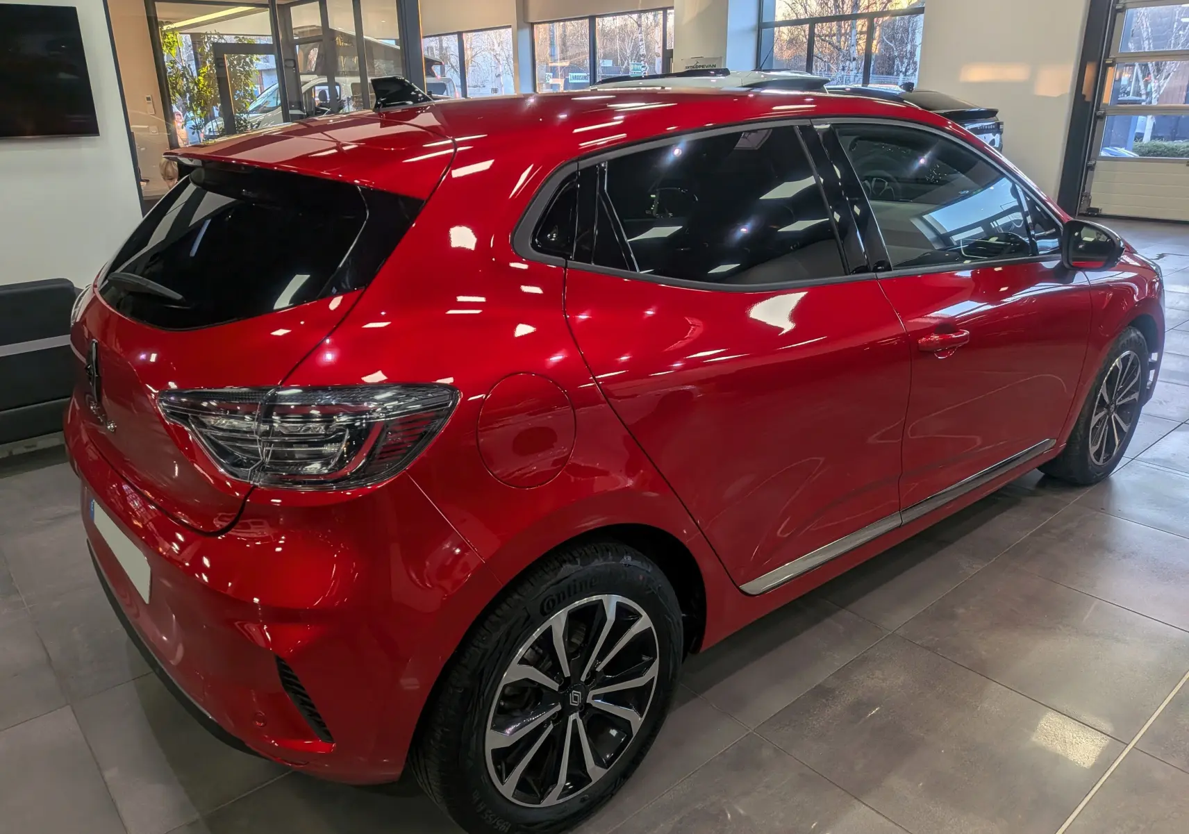 Renault Clio V Rouge Flamme vue 3/4 arrière droit en intérieur, avec jantes alliage bicolores et vitres teintées.