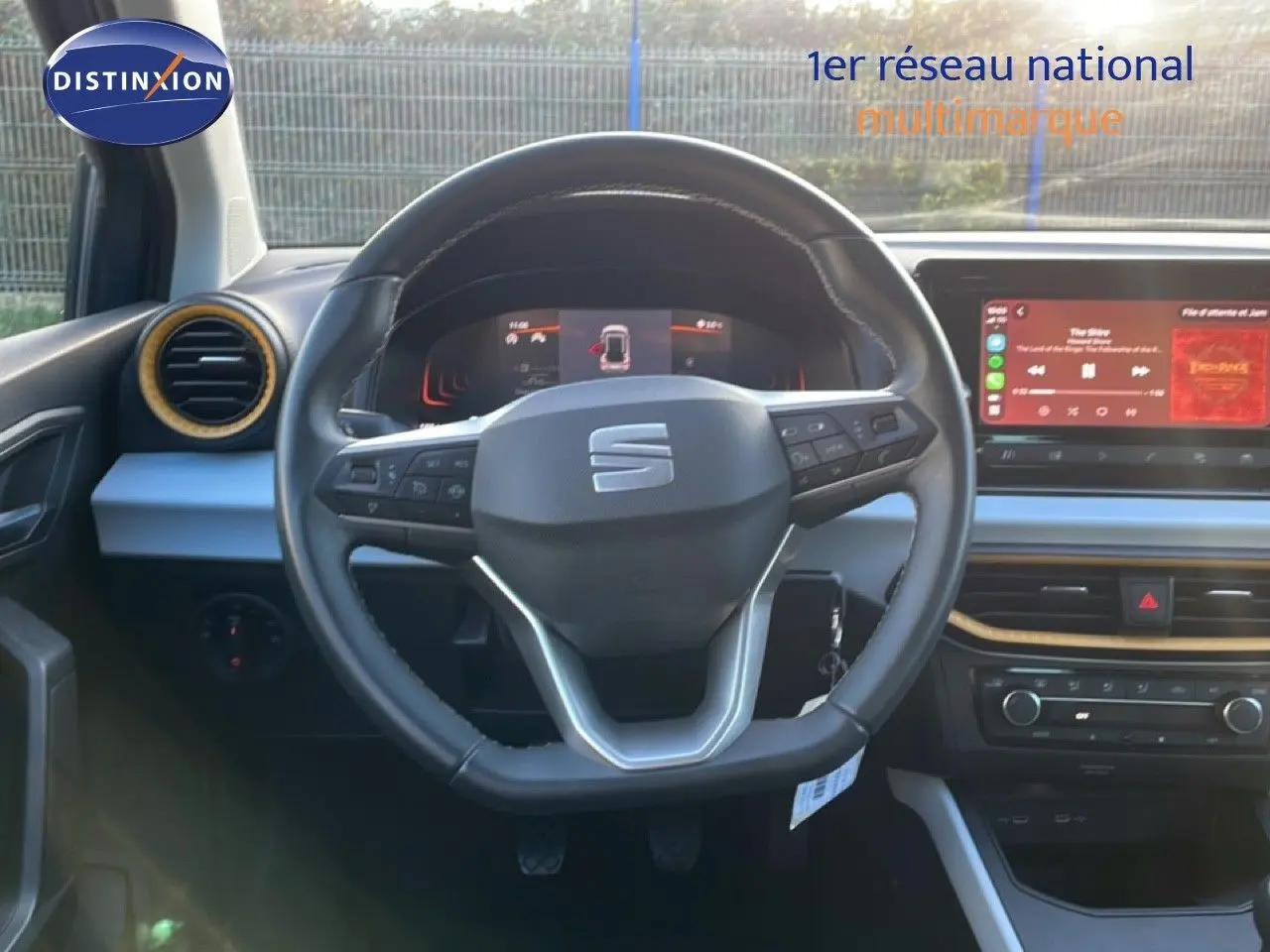 Vue intérieure centrée sur le volant noir d’une SEAT Arona gris fiord avec toit blanc, tableau de bord et écran tactile visibles.