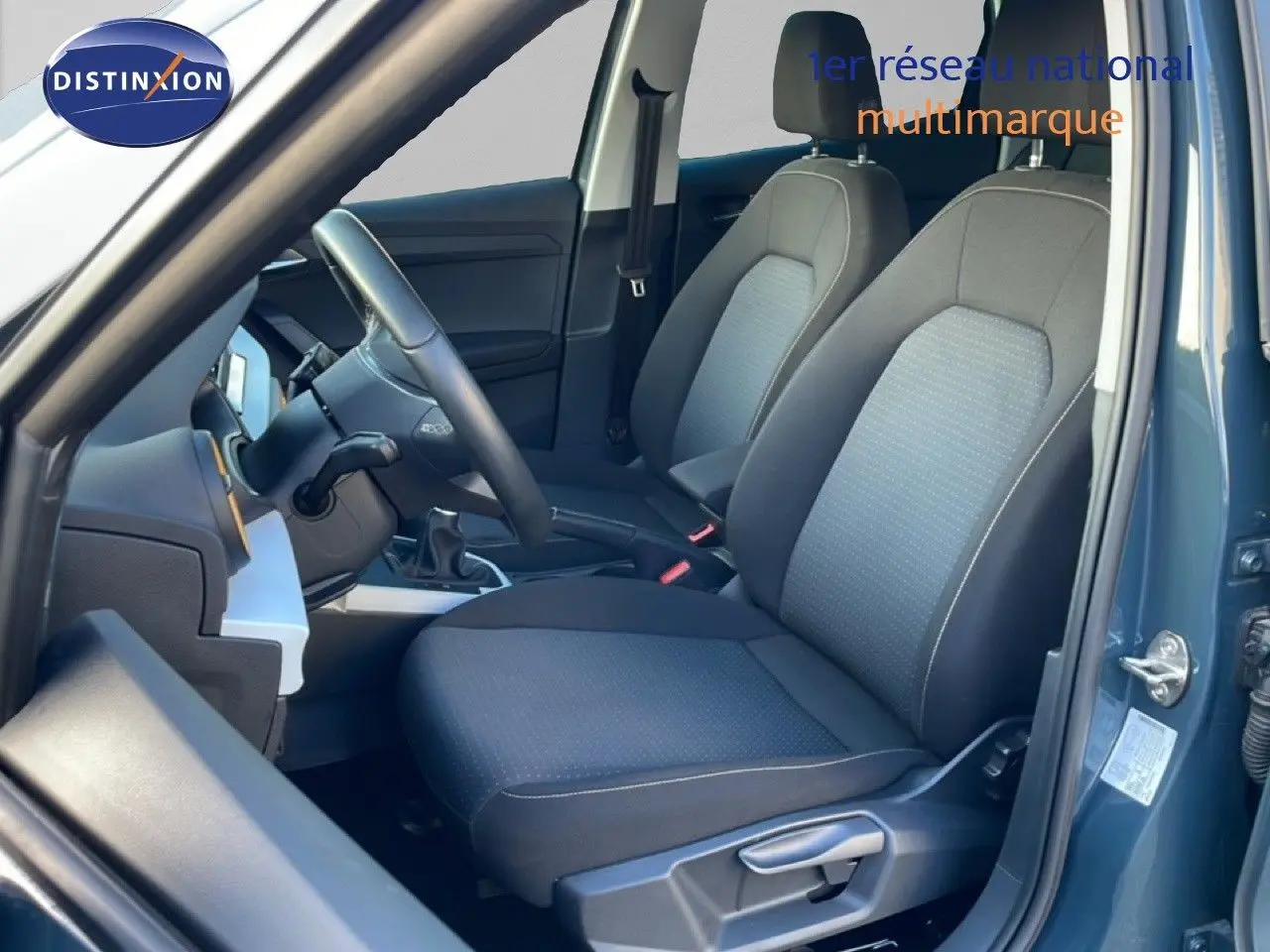 Vue intérieure côté conducteur du SEAT Arona gris Fiord, montrant les sièges tissu noir et la boîte manuelle.