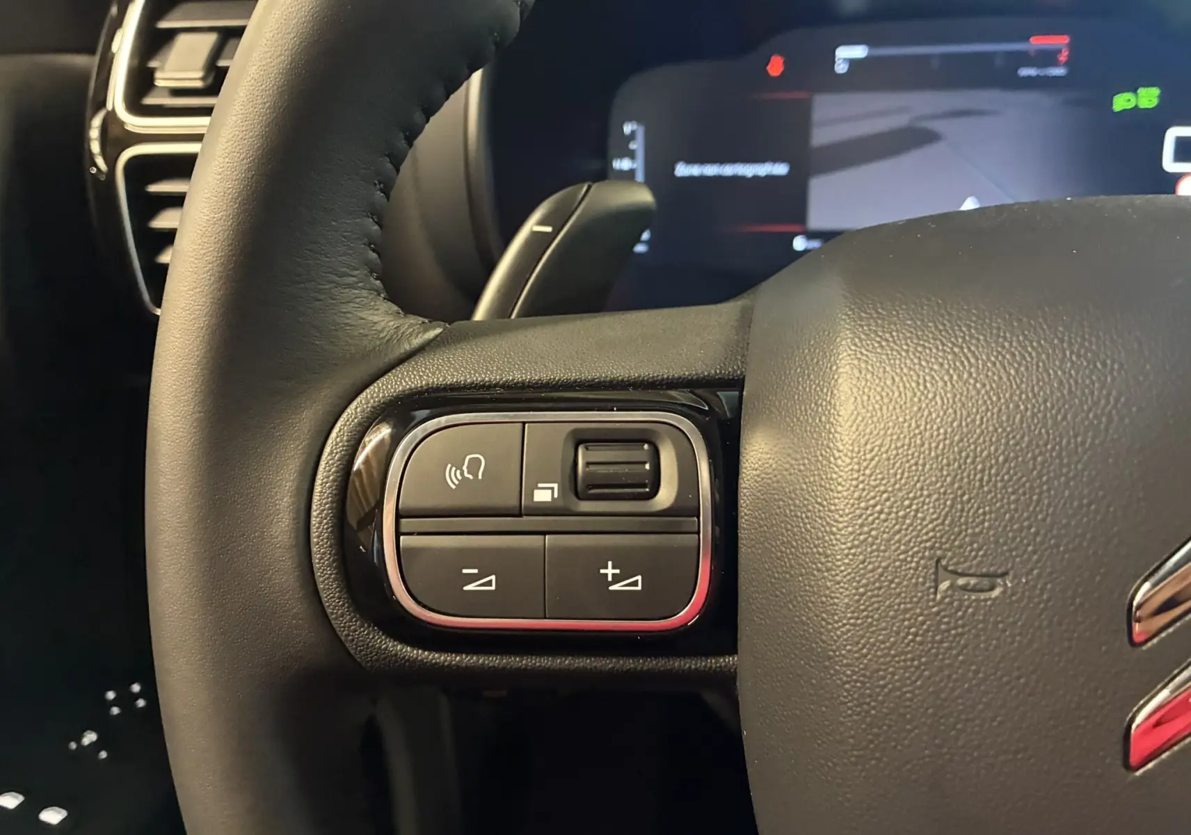 Gros plan sur les commandes gauche du volant en cuir noir du Citroën C5 Aircross 2025, affichage numérique en arrière-plan.